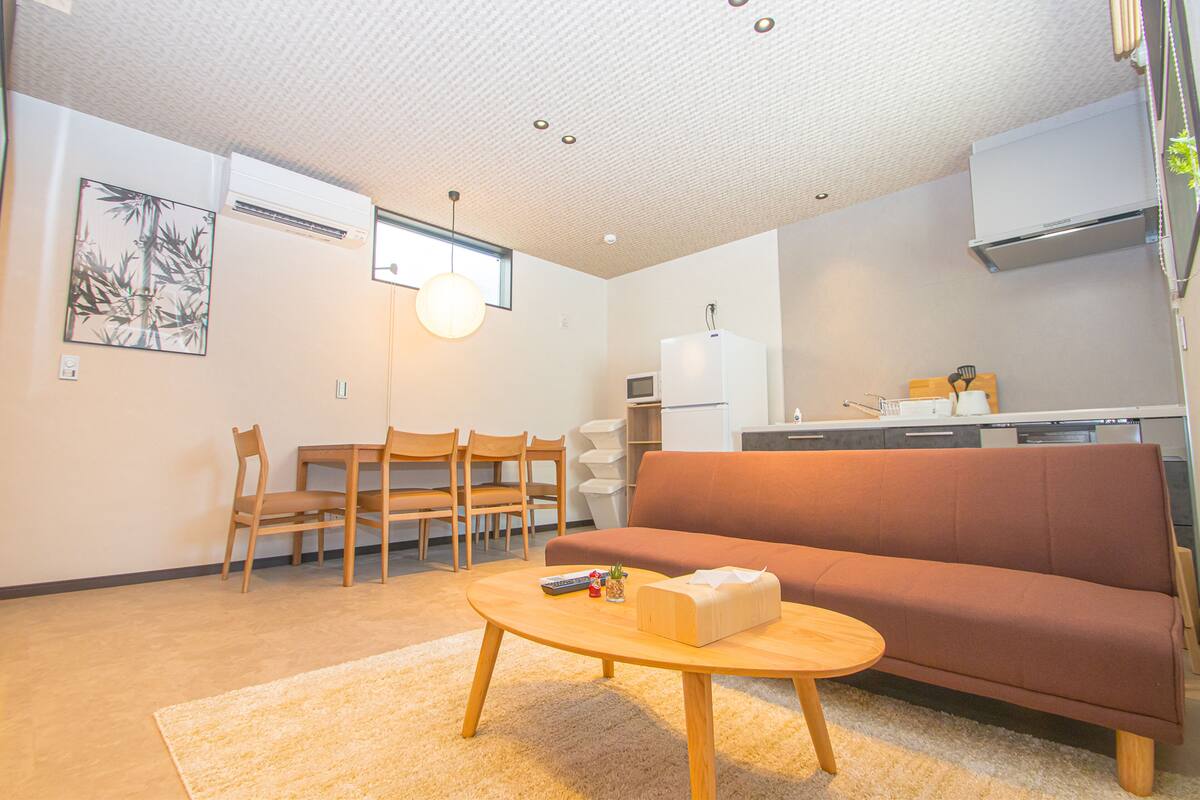 Un espacio habitable compacto con sofá, una zona de comedor con sillas, una cocina equipada e iluminación empotrada en el techo.