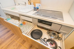 A kitchen with a built-in stove, a dishwasher, and a drawer with dishes and cookware.