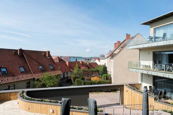 A modern building with a flat roof, a balcony with glass railings, and a landscaped area with plants and seating. - Milchhändler Zock Suite - Farm Suites ID Object 123476 (Waren (Müritz))