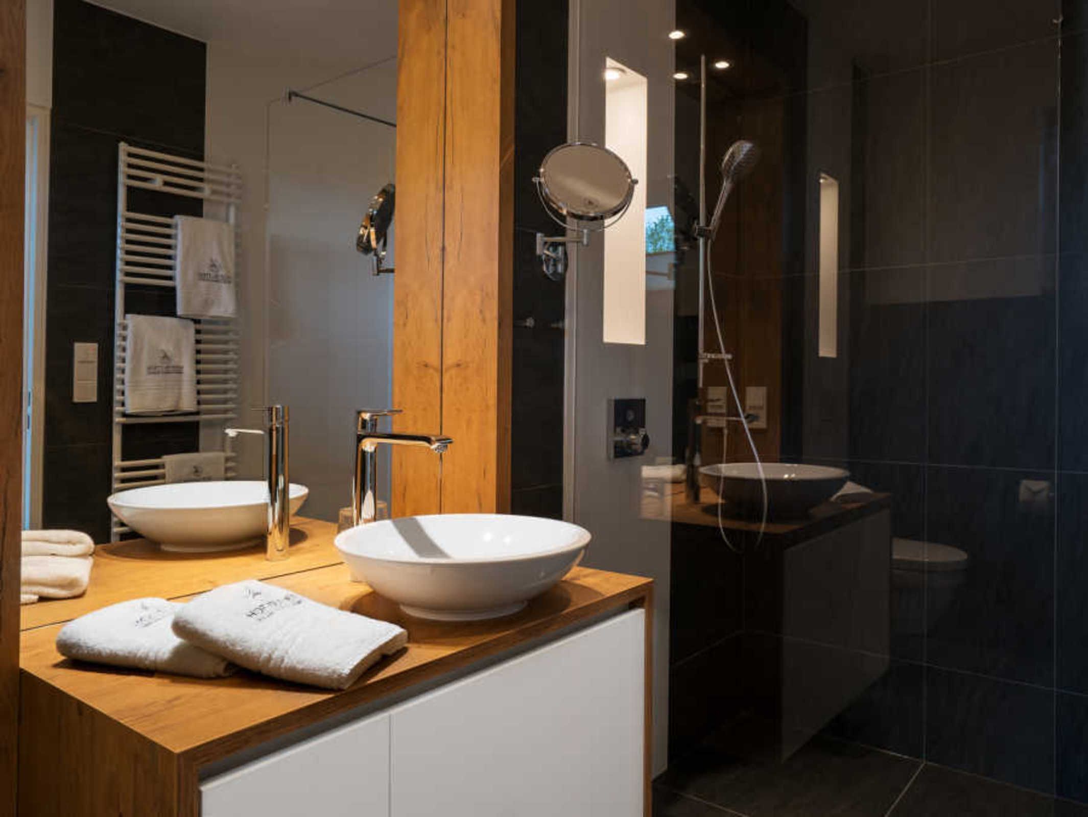 A modern bathroom with two large white sinks, a wooden vanity, a mirror, and a glass-enclosed shower area.