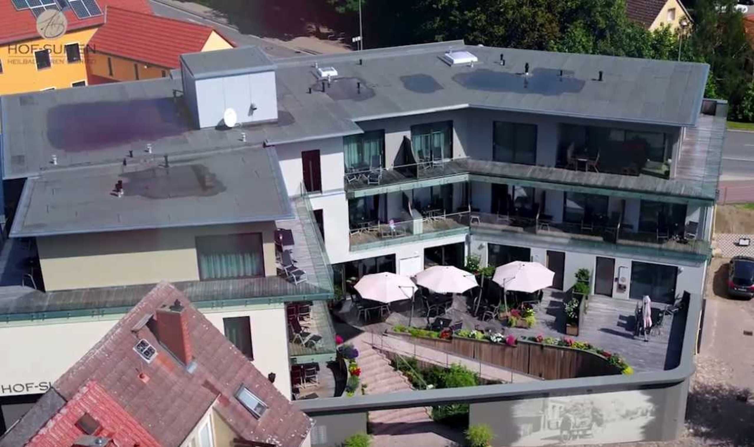 A modern building with a glass facade, outdoor seating area, and a rooftop terrace.