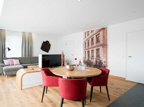 Un salon moderne avec une table ronde en bois, des chaises rouges, un canapé gris et un téléviseur à écran plat.