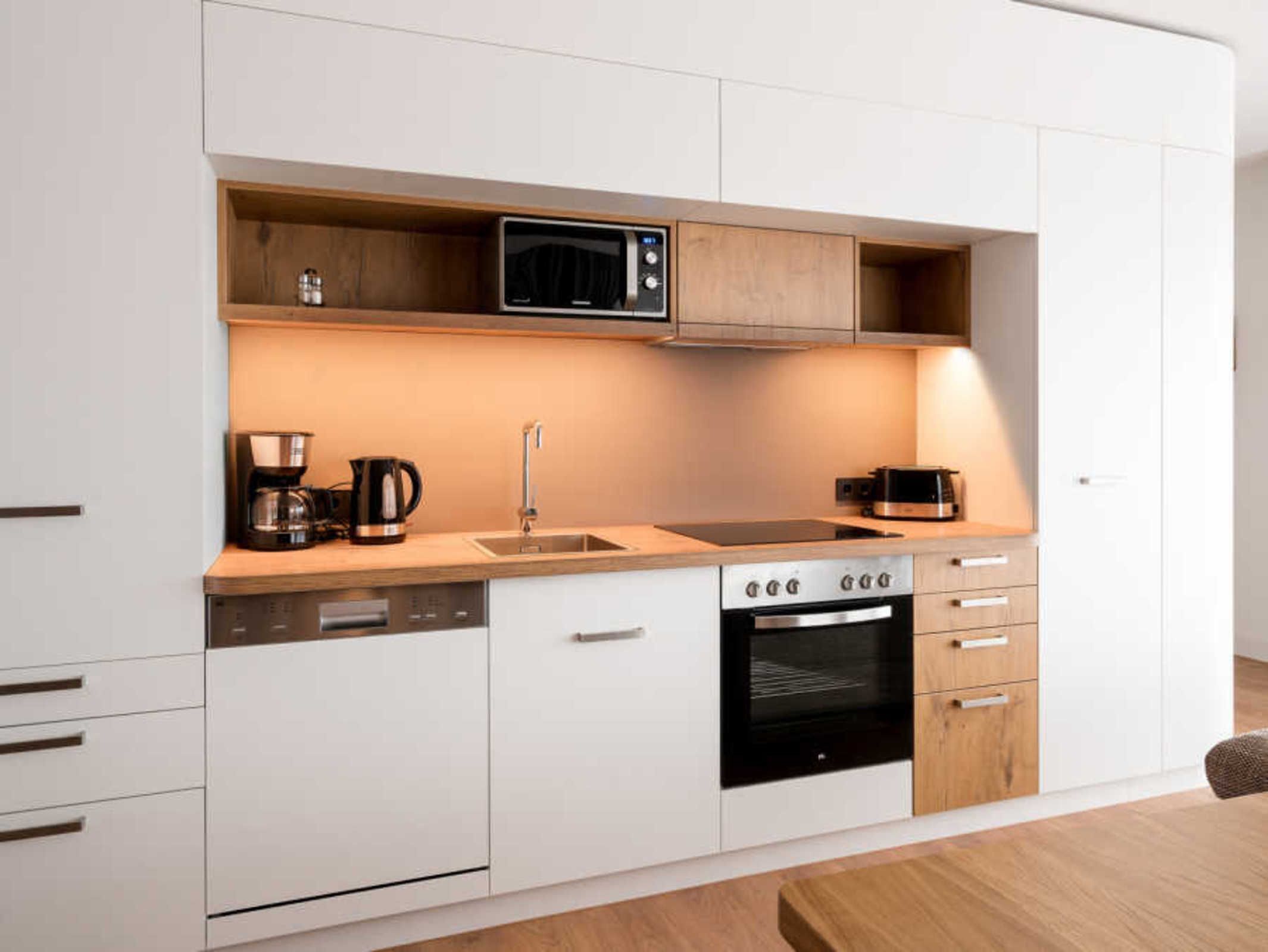 A modern kitchen with white cabinetry, a built-in microwave, a coffee maker, a sink, and an oven.