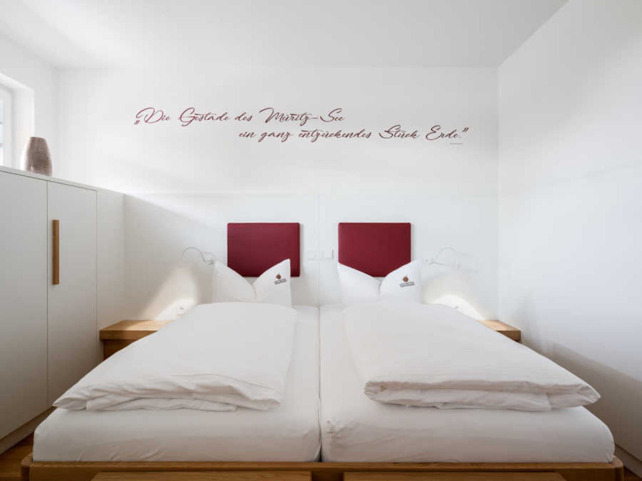 Ein Doppelbett mit weißer Bettwäsche, zwei Nachttische und eine Wand in Rot.