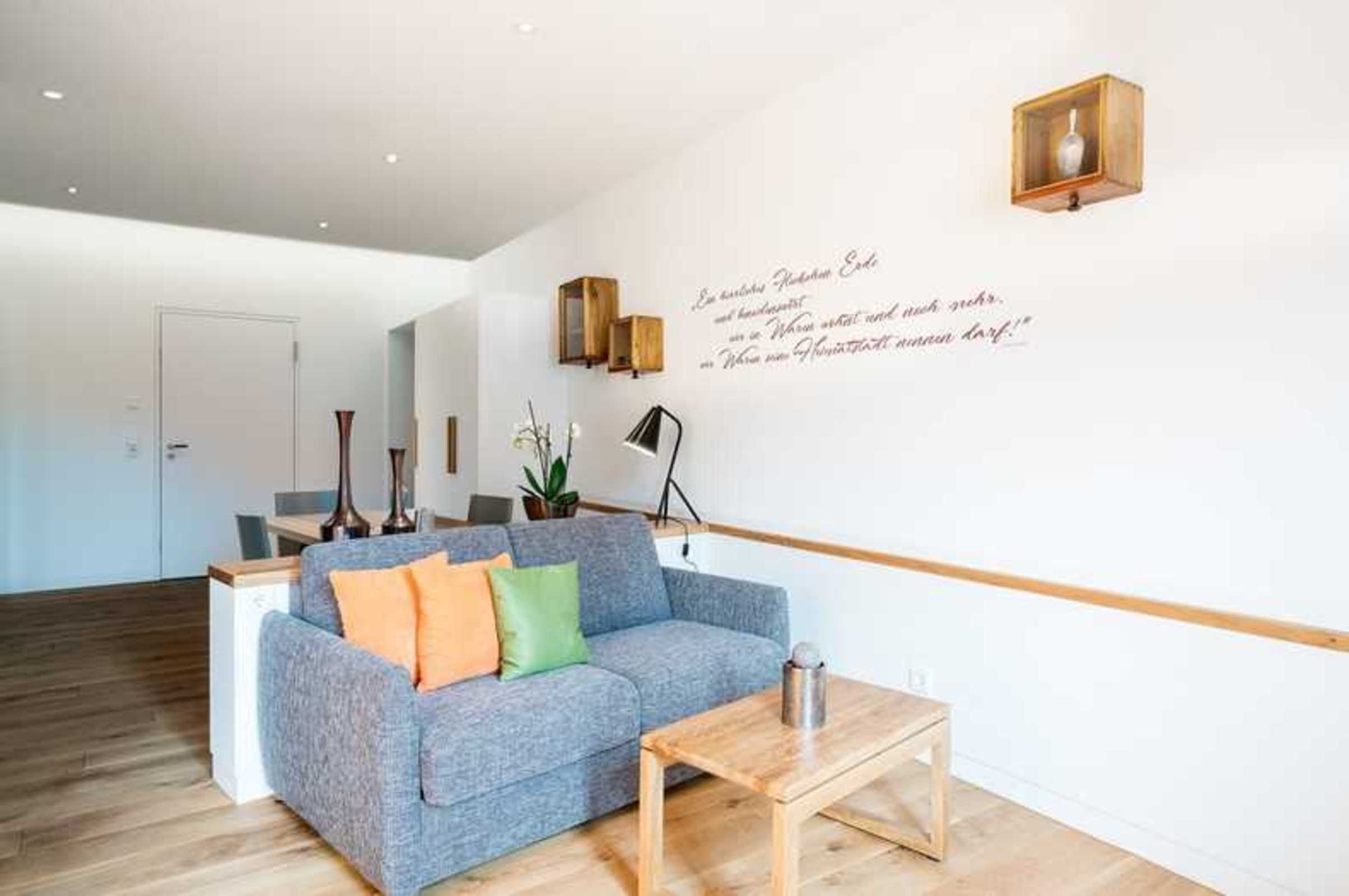 A modern living room with a grey sofa, wooden coffee table, and a wall-mounted light fixture.