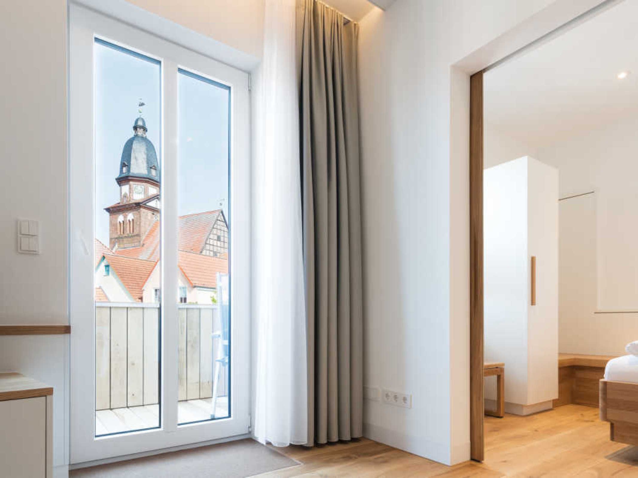 A modern room with a large sliding glass door leading to a balcony, a wooden floor, and a bed with a wooden headboard.