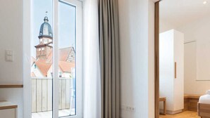 Una habitación moderna con un amplio ventanal corredero que da a un balcón, piso de madera y una cama con cabecera de madera.