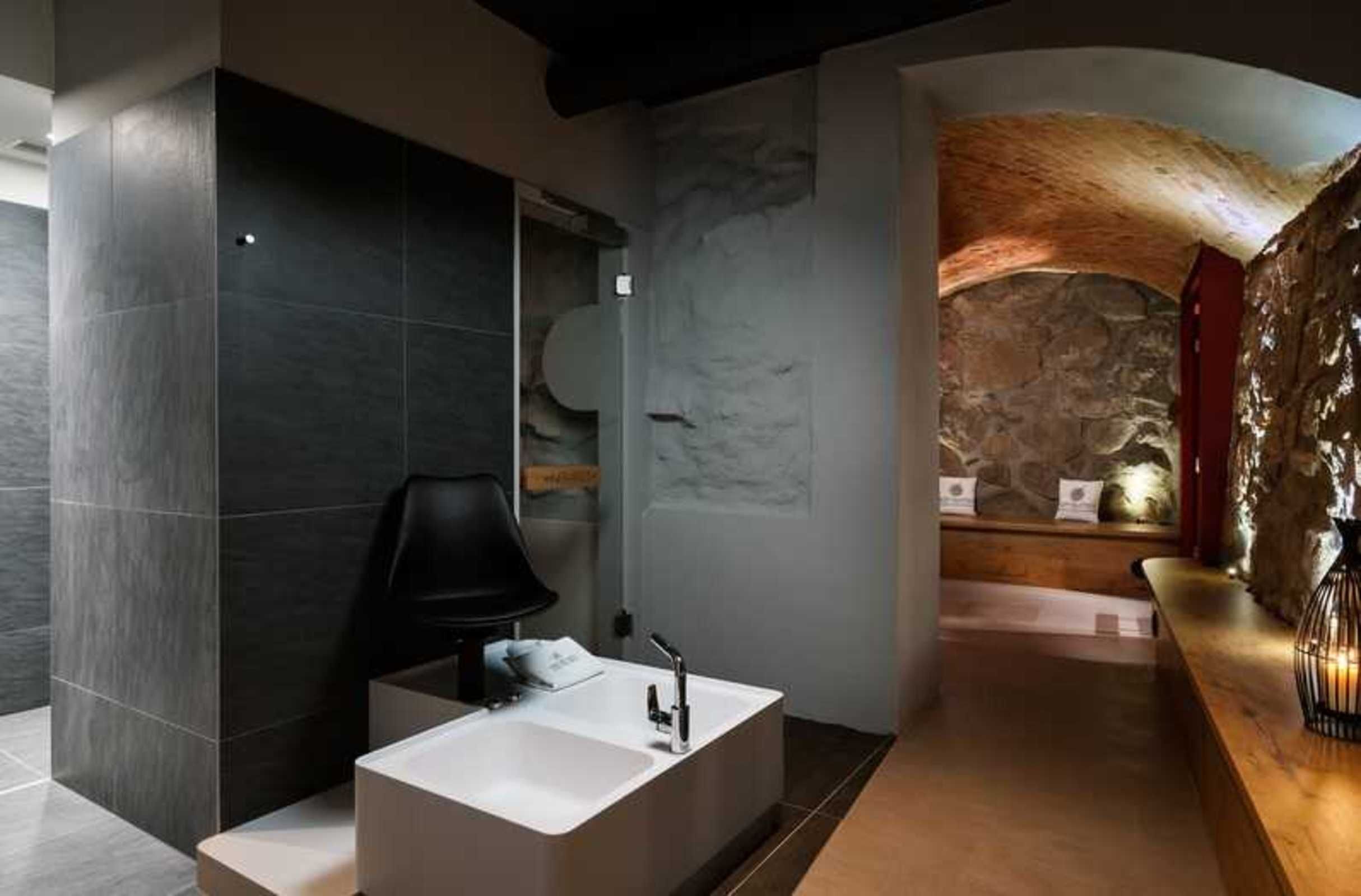 A modern bathroom with a large white sink, dark tiled walls, and a stone accent wall.