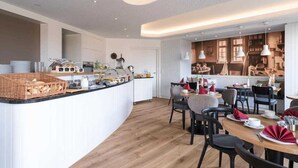 A modern kitchen with a central island, dining area with tables and chairs, and a wall displaying various kitchen items.