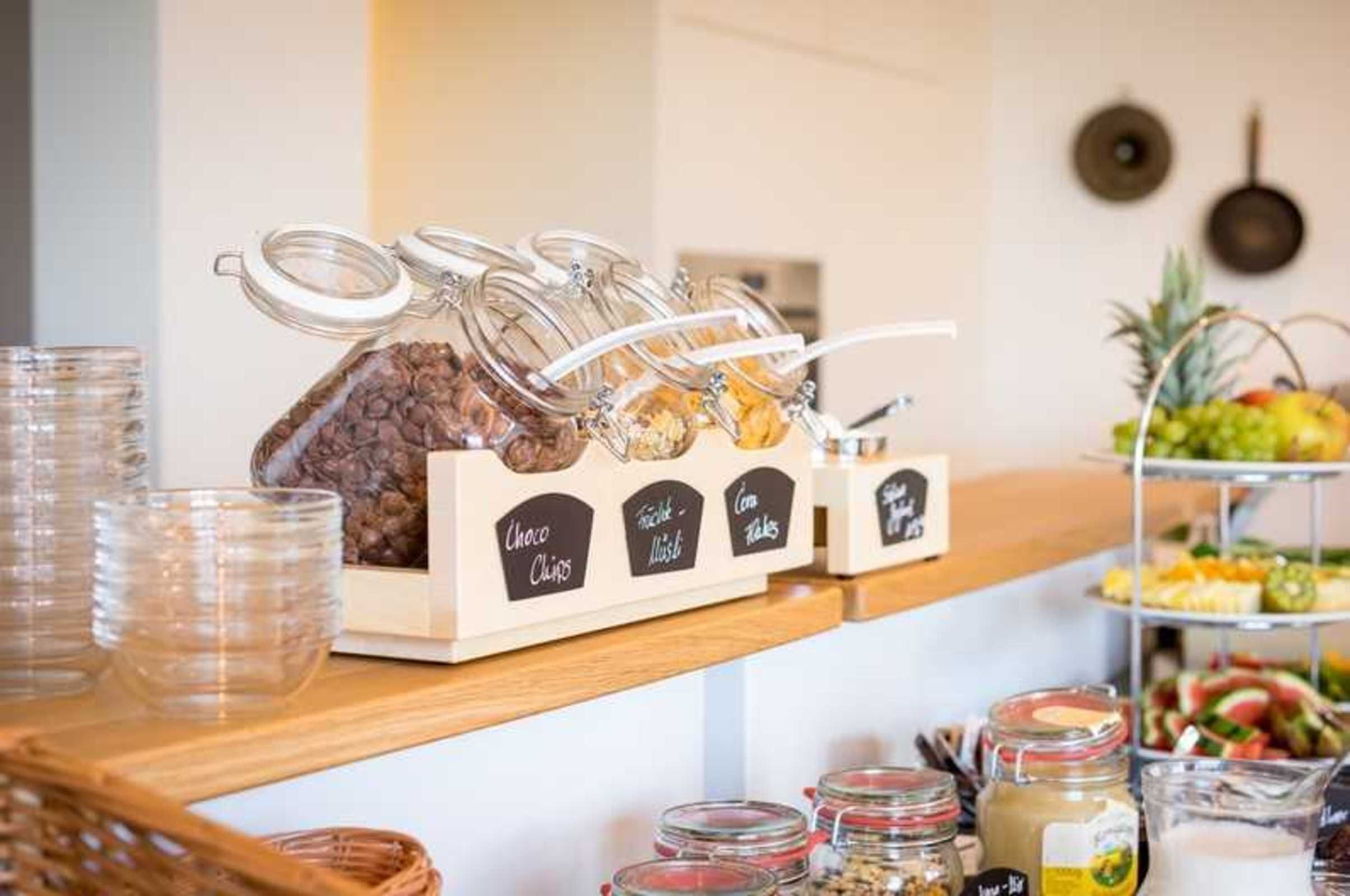 Un buffet avec des récipients étiquetés contenant des en-cas tels que des pépites de chocolat, un mélange de fruits, des céréales de maïs et du yaourt.