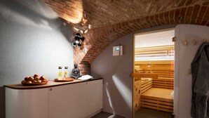 A small, cozy room with a brick ceiling, a sauna, and a kitchenette with a fruit bowl and bottles.