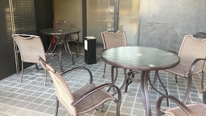 Un espace patio avec une table ronde en verre et des chaises en osier, une poubelle et un mur à texture.