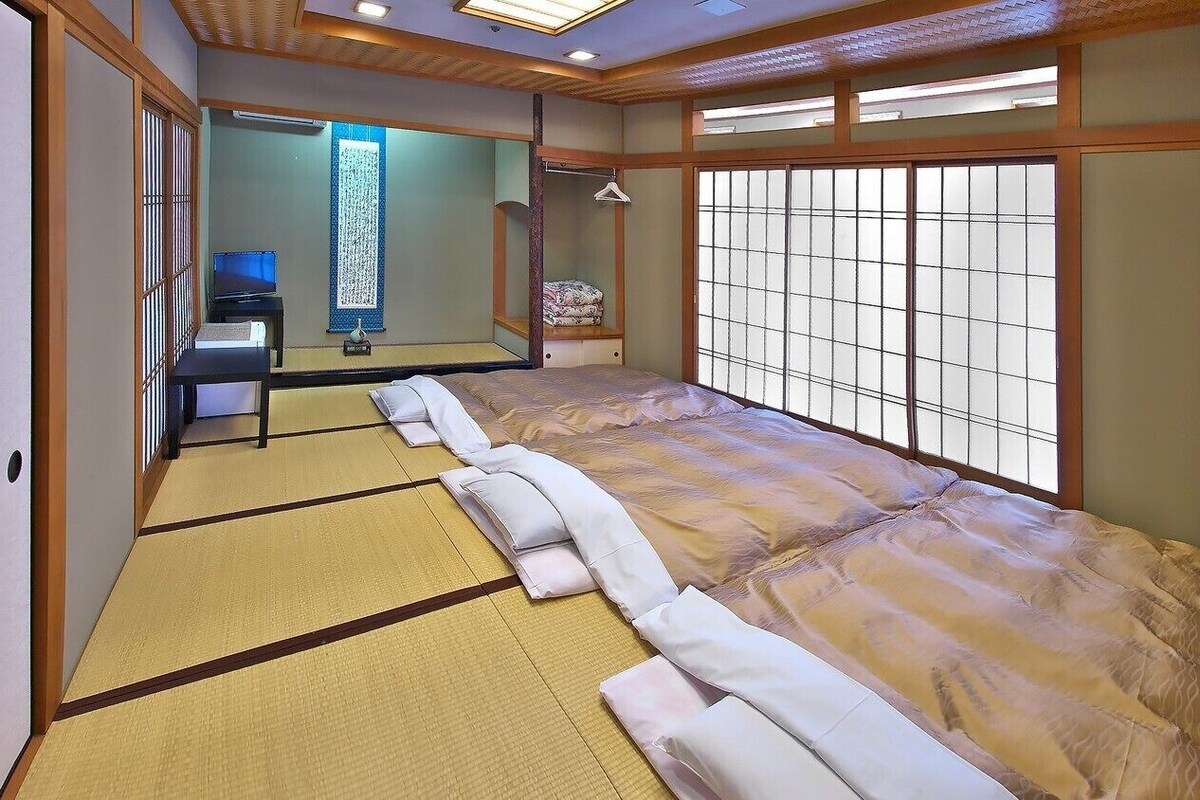 A traditional Japanese-style room with tatami flooring, a futon bed, a television, and sliding doors.