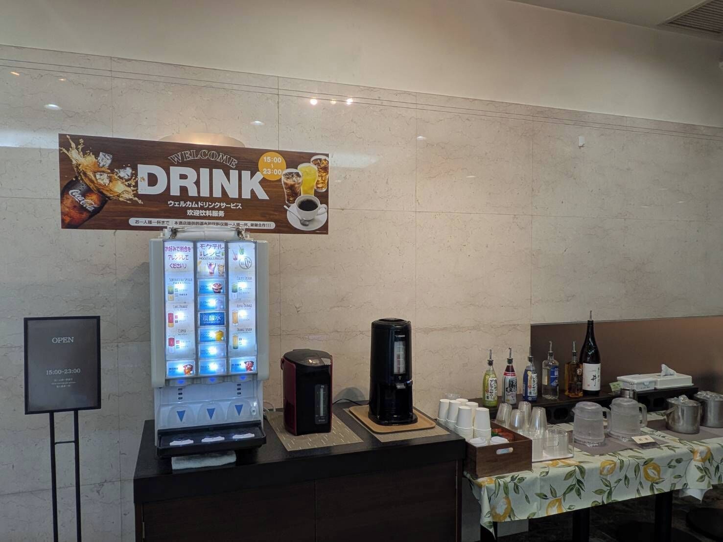 A beverage station with a Coca-Cola advertisement, a drink vending machine, and a coffee maker.