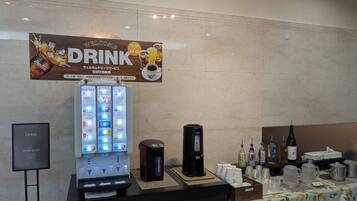 A beverage station with a Coca-Cola advertisement, a drink vending machine, and a coffee maker.