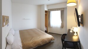 Une chambre d’hôtel comprenant un lit, un bureau avec une lampe, une chaise, une fenêtre avec des rideaux et un téléviseur fixé au mur.