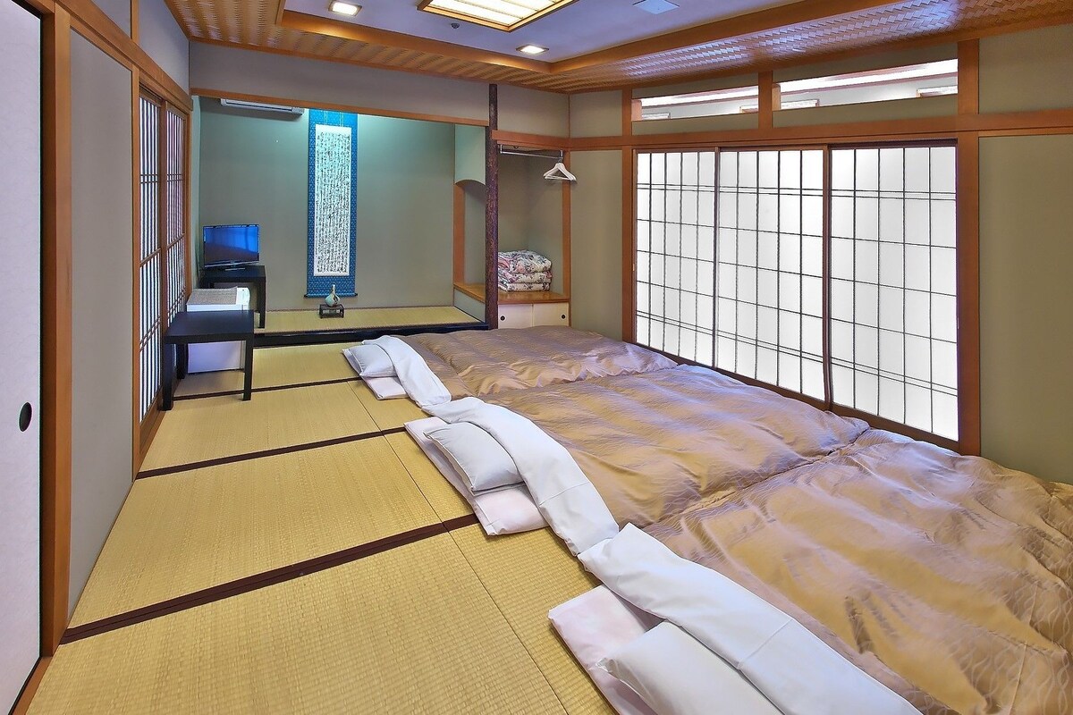 A traditional Japanese room with tatami flooring, a futon bed, a shoji screen, and a small desk with a chair.
