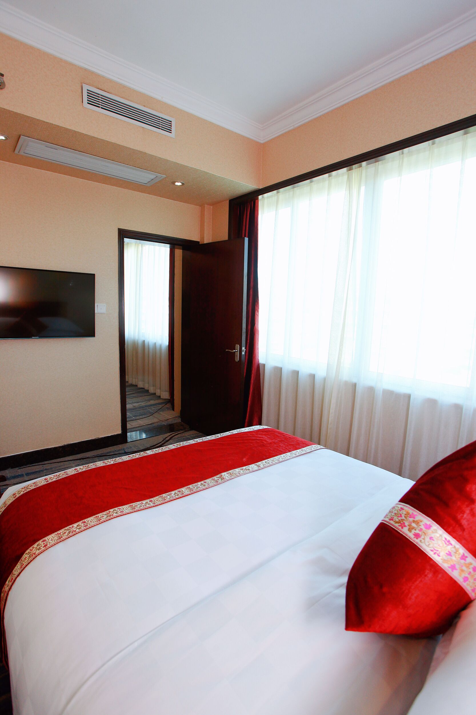 Una camera d'albergo con un letto grande, una televisione a parete e una finestra con tende.