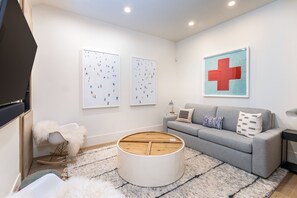 Uma sala de estar moderna com um sofá cinzento, uma mesa de centro redonda e obras de arte nas paredes.