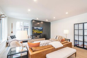 A modern living room with a sofa, a glass coffee table, a flat-screen TV, and a bookshelf.