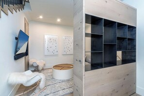 A modern interior with a staircase, a white chair with a fluffy cushion, a round wooden table, and a black shelving unit.