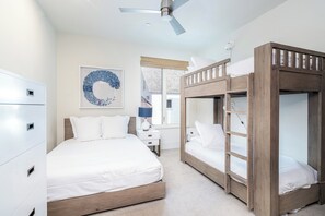 Un dormitorio con una cama litera, una cama individual, un ventilador de techo, una mesita de noche y una obra de arte colgada en la pared.