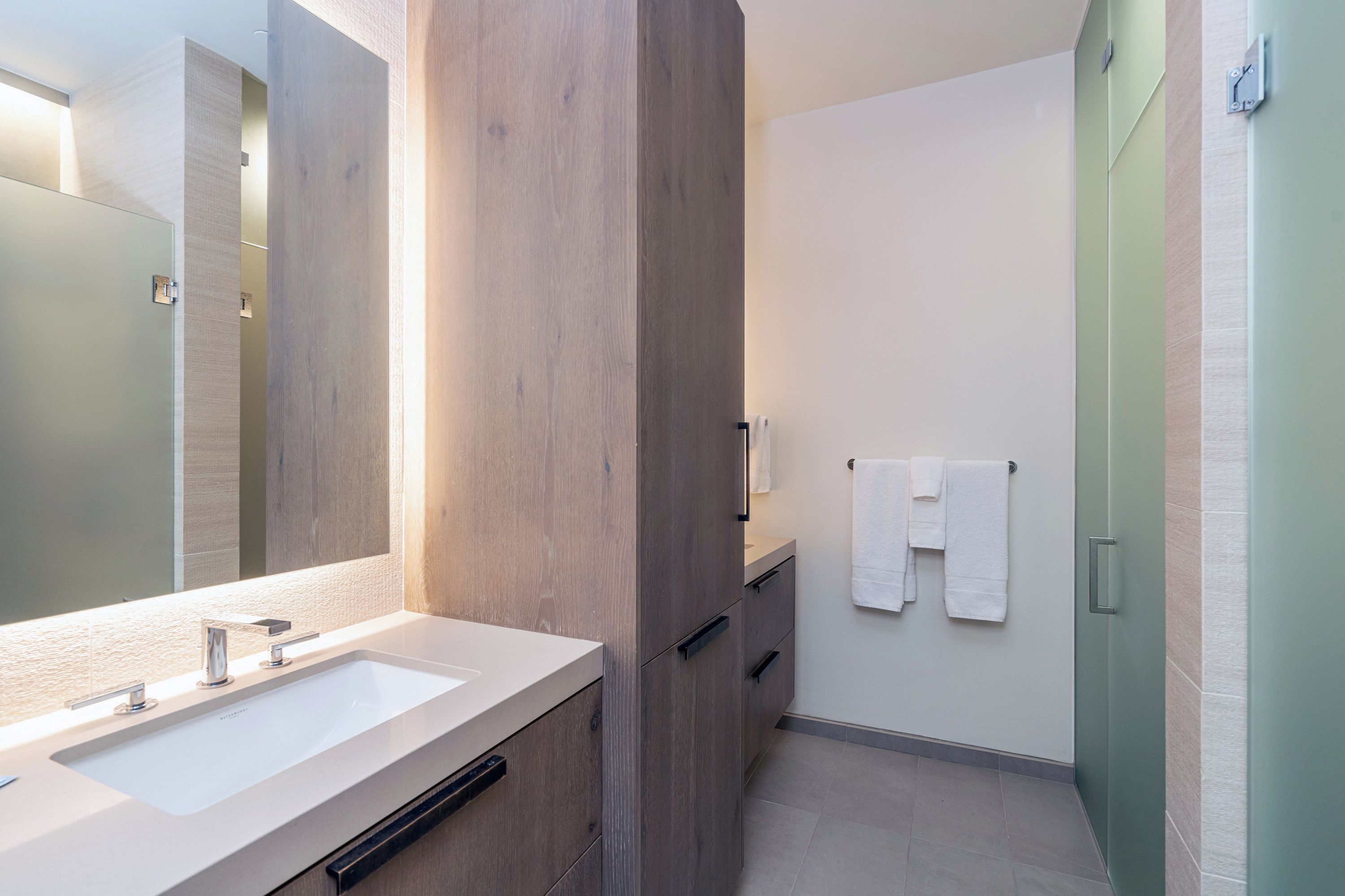 A modern bathroom with a large mirror, two sinks, and a shower area.