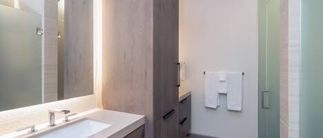 A modern bathroom with a large mirror, two sinks, and a shower area.