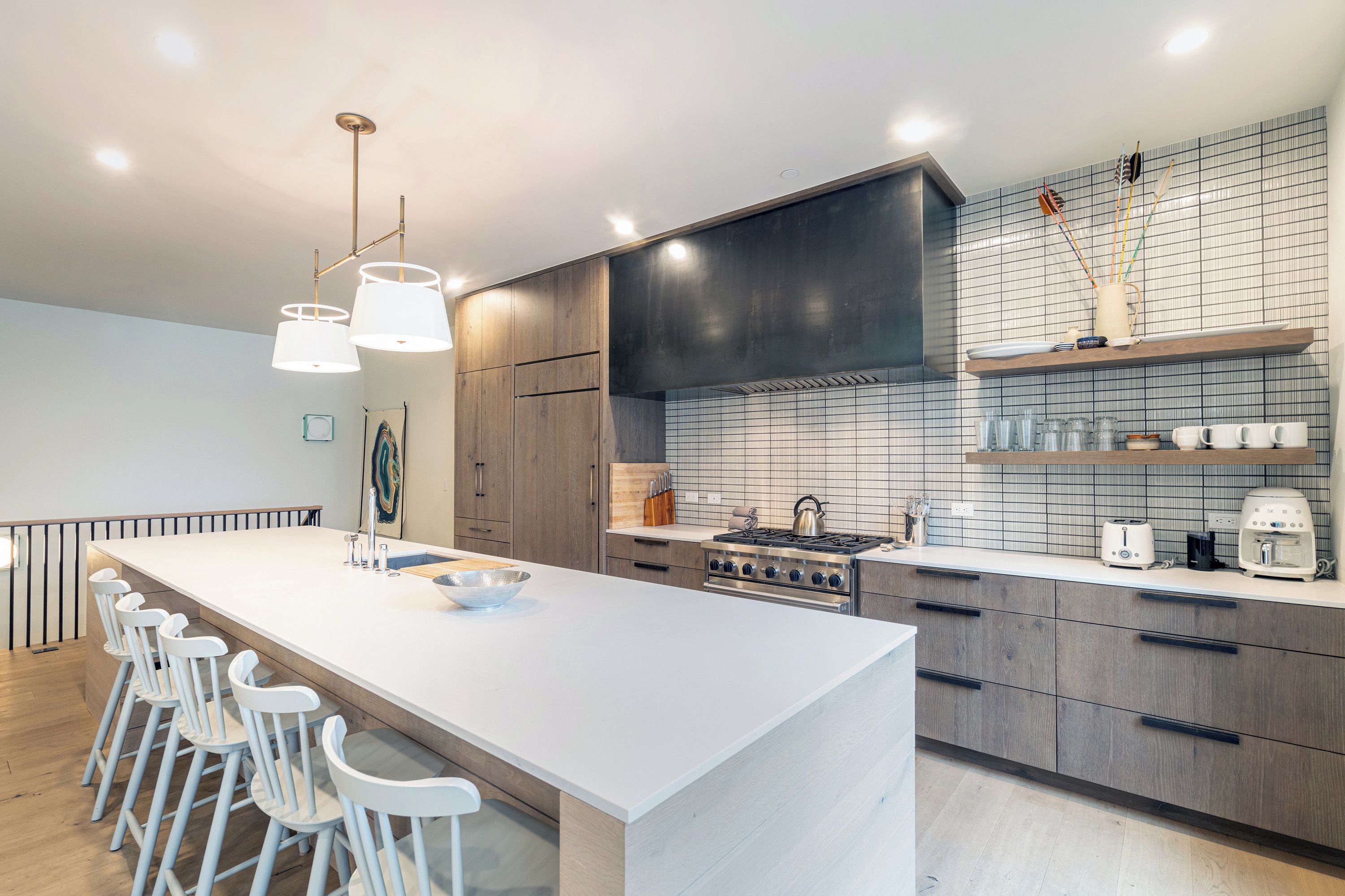 A modern kitchen with a central island, bar stools, a stove, and a tiled backsplash.