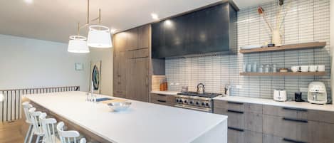 A modern kitchen with a central island, bar stools, a stove, and a tiled backsplash.