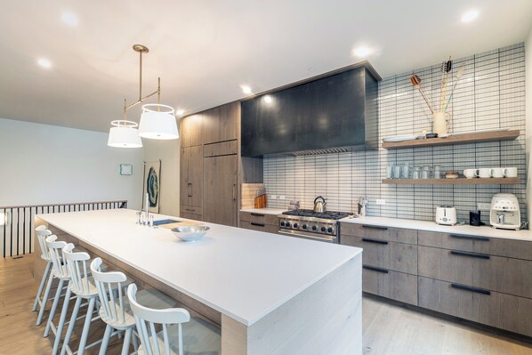 A modern kitchen with a central island, bar stools, a stove, and a tiled backsplash.