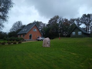 Une maison en briques avec un toit en pente, une voiture garée devant et un gros rocher au premier plan.