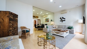 A modern living room with a sofa, coffee table, and wicker chair. There is a dining area in the background with a table and chairs. - Deluxe Penthouse Giralda Views, 3Bd 2Bt, 7 people, Parking optional (Sevilla)