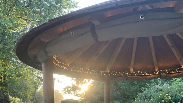 Een houten terras met een tafel met glazen blad en paars gewatteerde zitplaatsen.