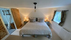 Een slaapkamer met een groot bed, twee nachtkastjes met lampen, een raam met gordijnen en een houten deur.