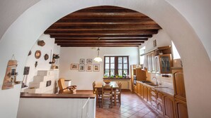 Una cocina con armarios de madera, una mesa de comedor con sillas, una lámpara colgante y una ventana con cortinas.