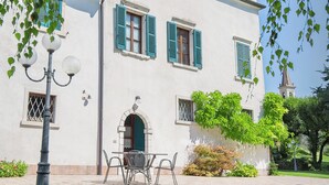 Un edificio blanco con contraventanas verdes, una entrada central y una torre de campanas al fondo.
