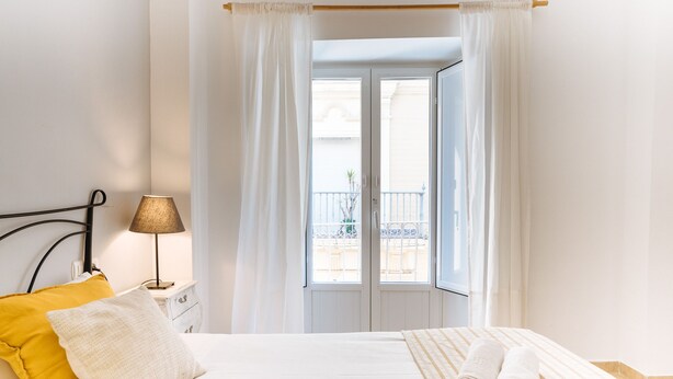 Une chambre à coucher avec un lit, une table de chevet, une lampe et une vue sur un balcon.