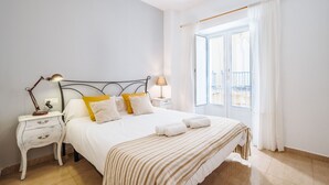 Un lit bien fait, recouvert d’une couvre-lit à rayures, une lampe de chevet et une table de chevet avec des tiroirs.
