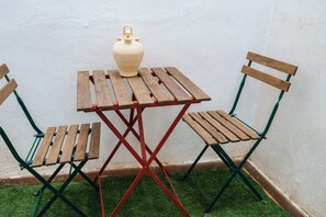 Ein kleiner Holztisch mit einer weißen Vase, zwei Holzstühlen und einem roten Metallgestell.