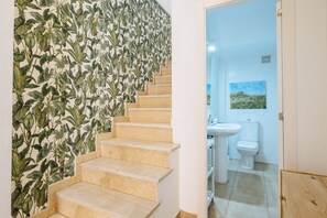 Eine Treppe mit botanischem Wandpapier, die zu einem Badezimmer mit Waschbecken und Toilette führt.
