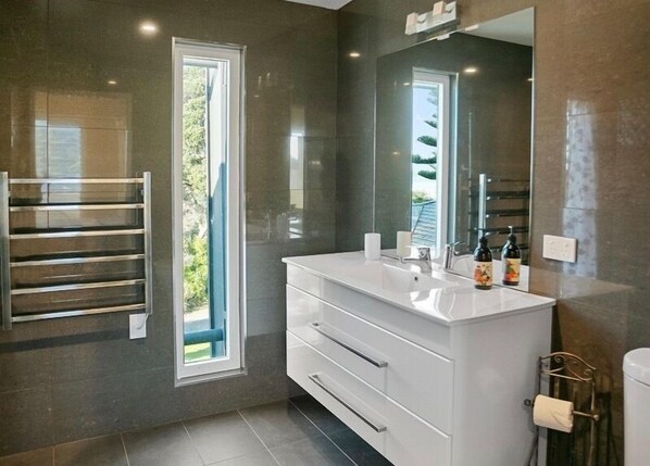 A modern bathroom with a large mirror, white vanity, and a towel rack.