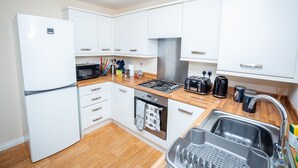 A compact kitchen with white cabinets, a built-in oven, a gas stove, a sink, and a refrigerator. - Grande Richesse Apartment (Coventry)