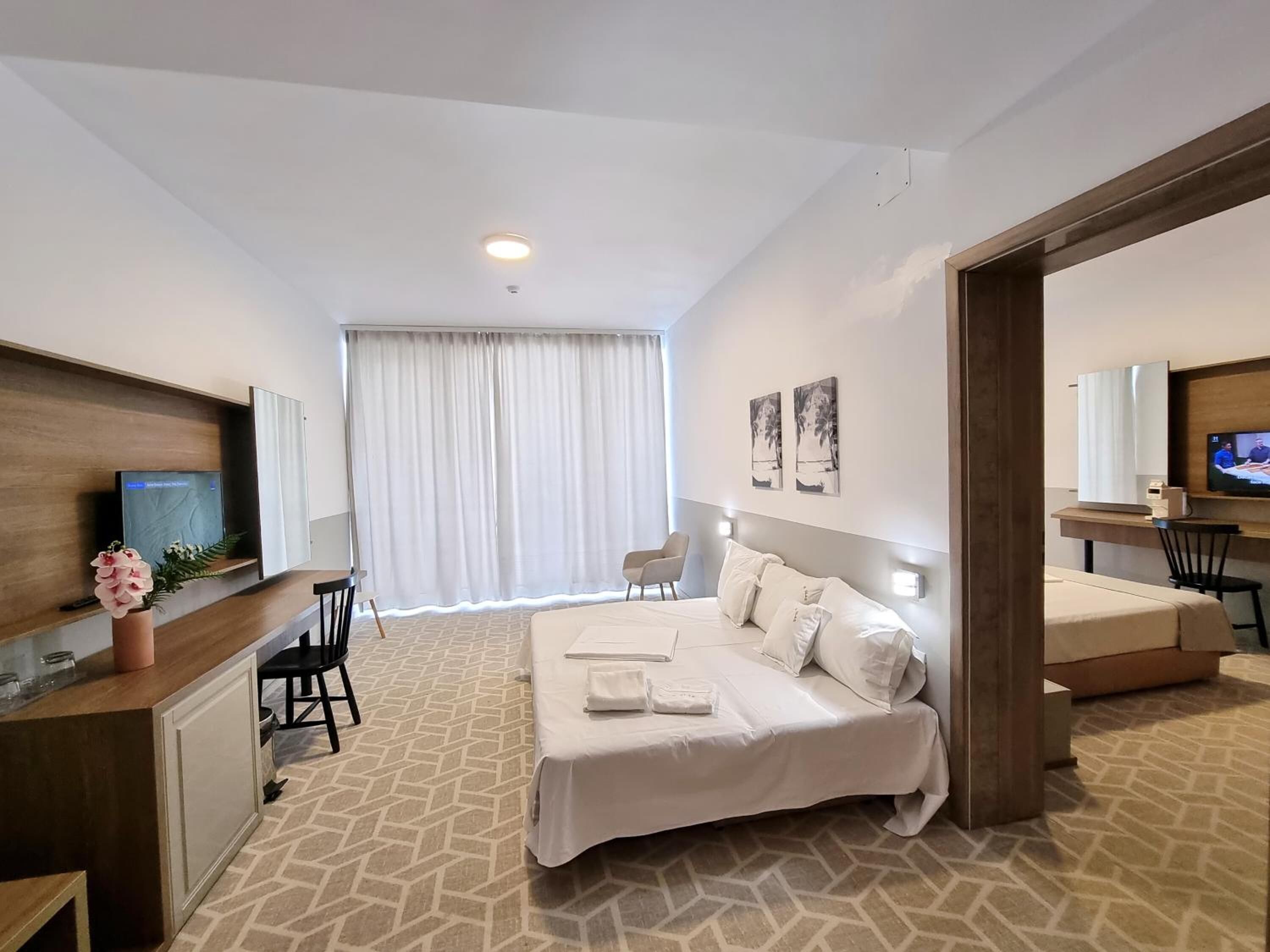 A hotel room with a bed, a desk, a chair, a television, and a window with curtains.