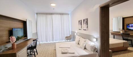 Habitación de hotel con cama, escritorio, silla, televisor y ventana con cortinas.