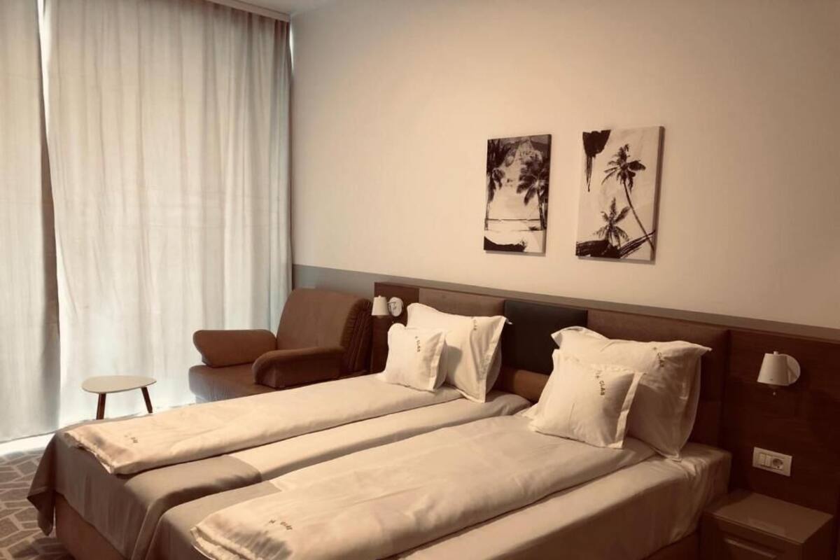 Una habitación de hotel con dos camas, una silla, una mesita pequeña y una obra de arte en la pared.