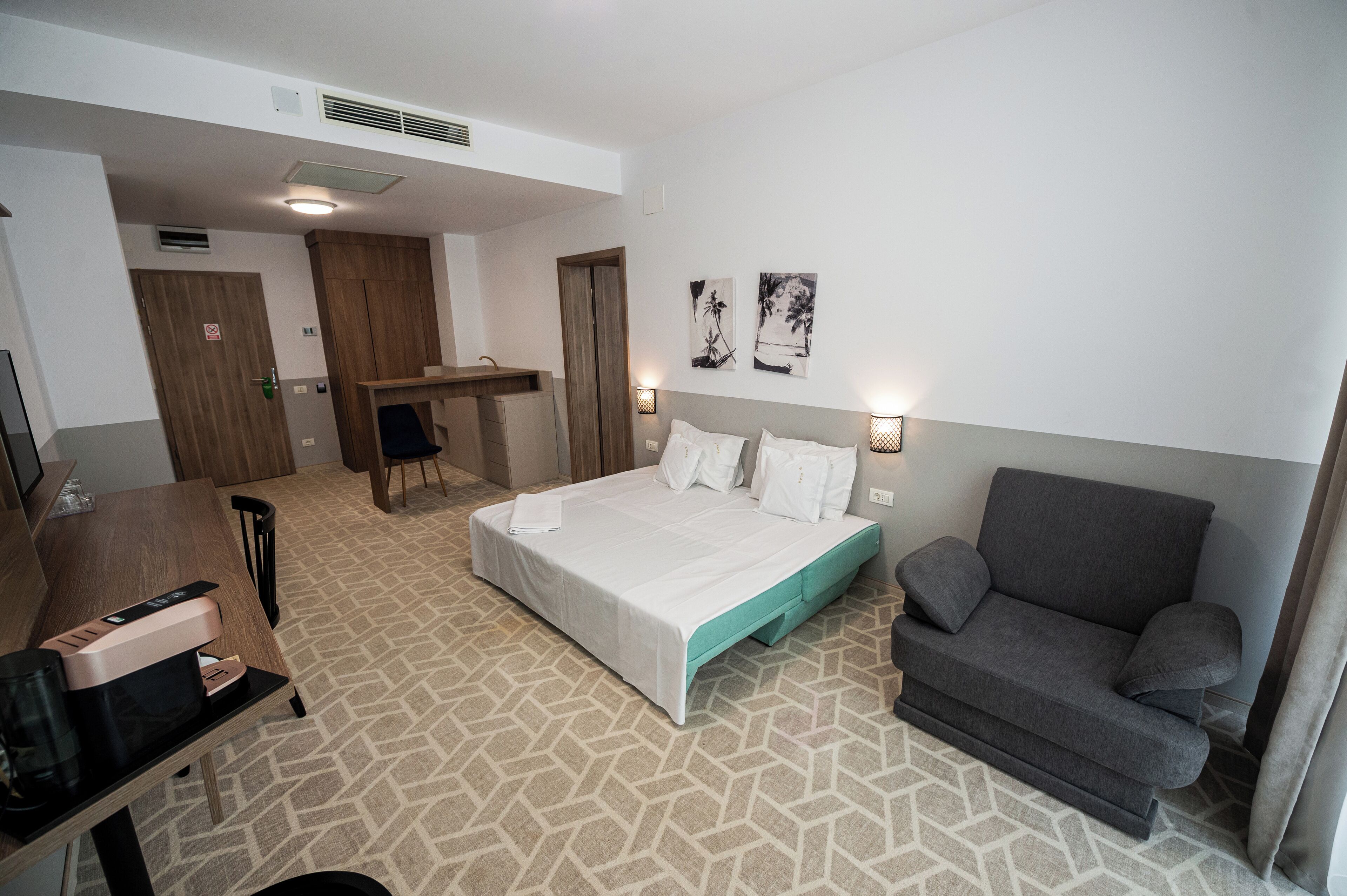 A hotel room with a bed, a desk with a printer, a sofa, and two wall-mounted lamps.