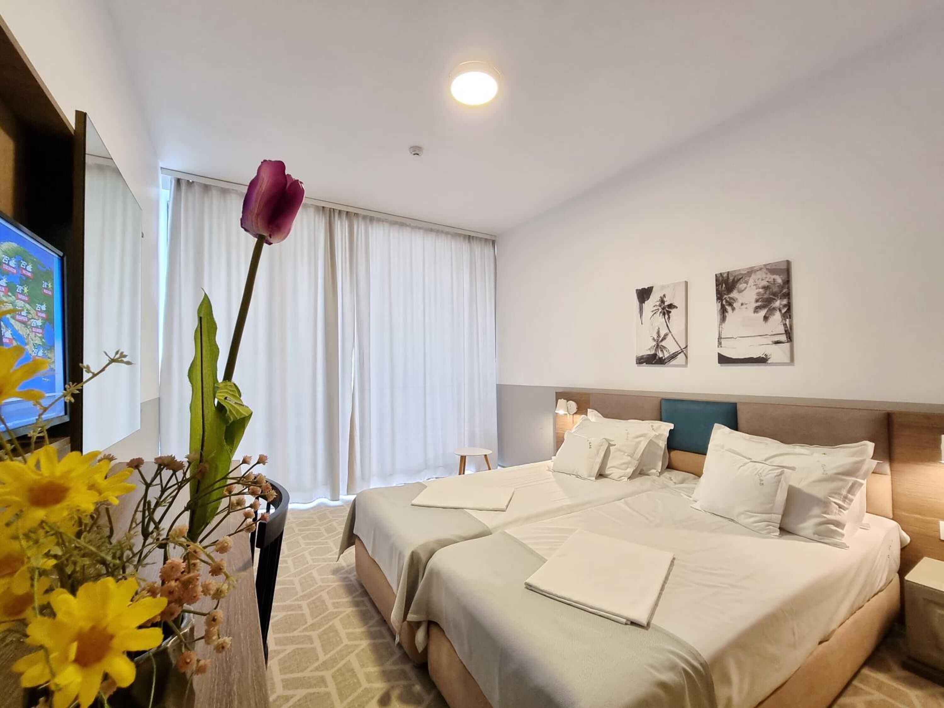 A hotel room with two beds, a TV, a vase with flowers, and two wall art pieces.