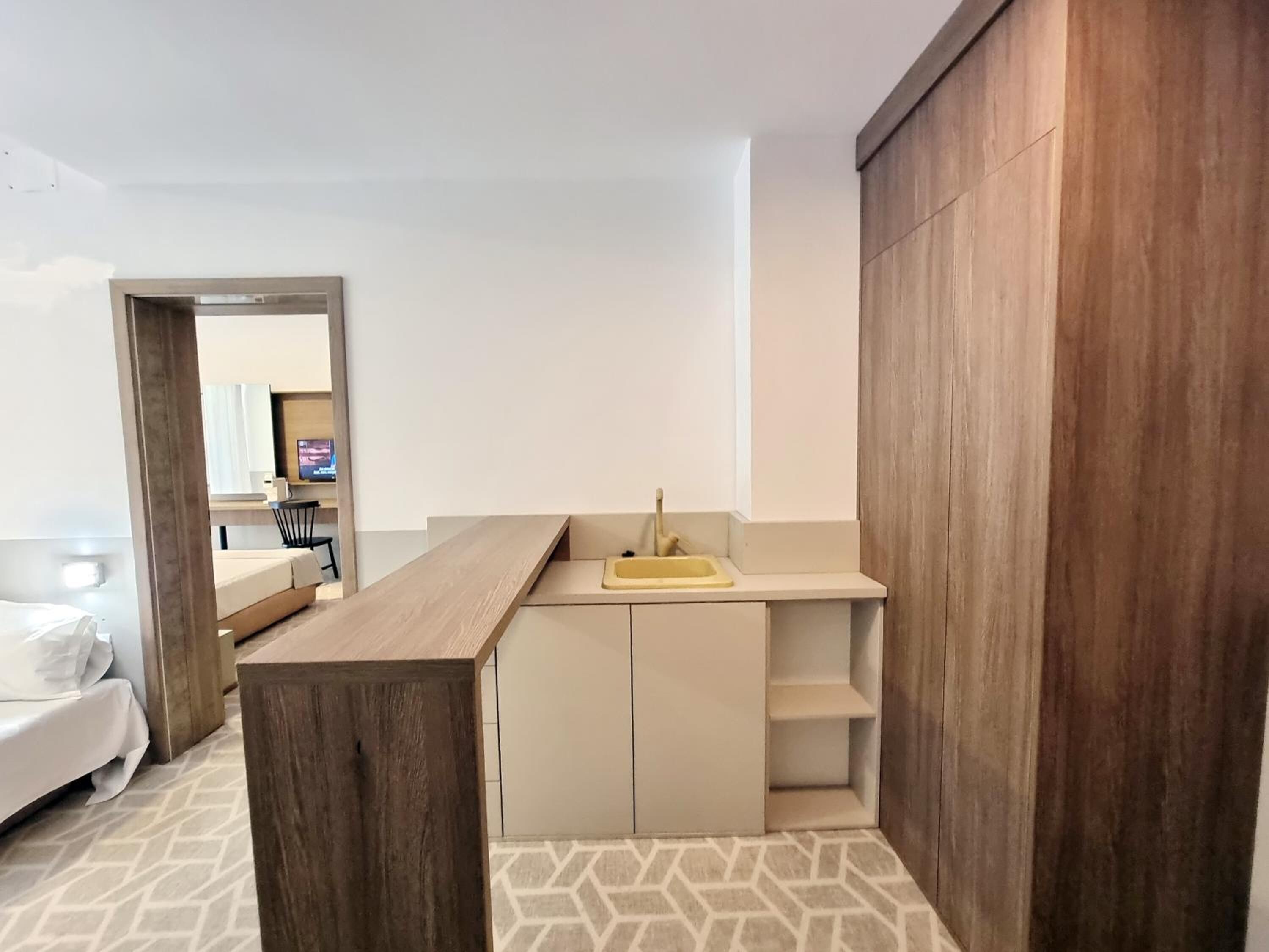 A modern hotel room with a wooden bench, a small sink, and a bed.