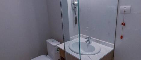A small bathroom with a toilet, a glass-enclosed sink, and a shower.